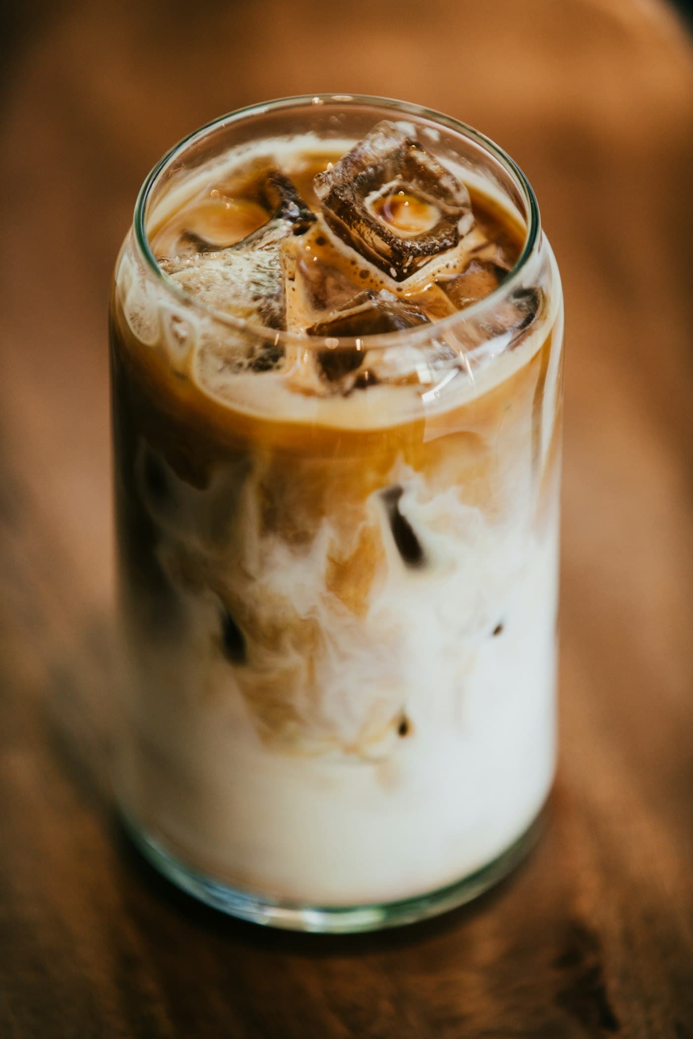 An iced latte in a tall glass on a walnut table