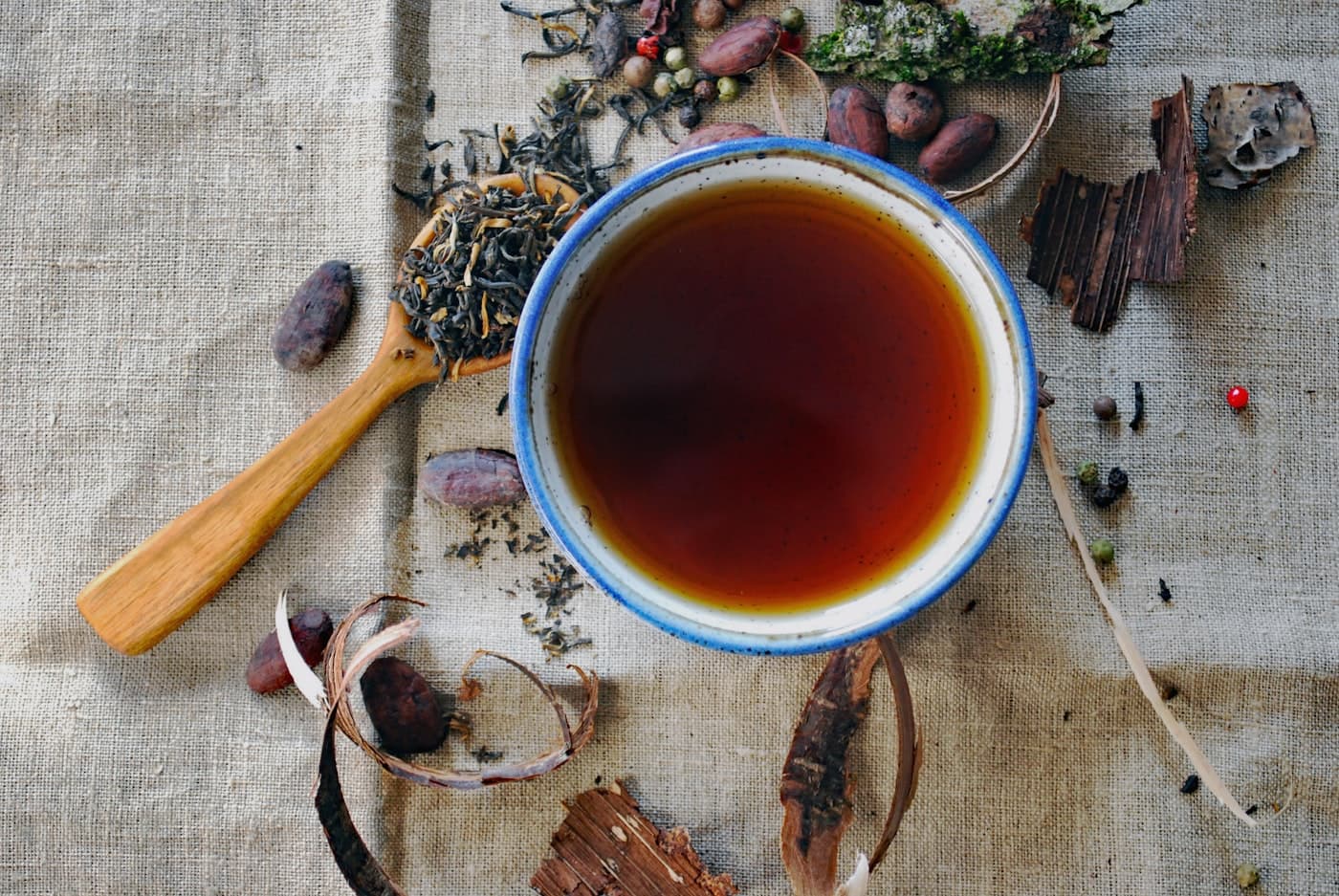 Masala chai in an enamel cup surrounded by whole spices on linen