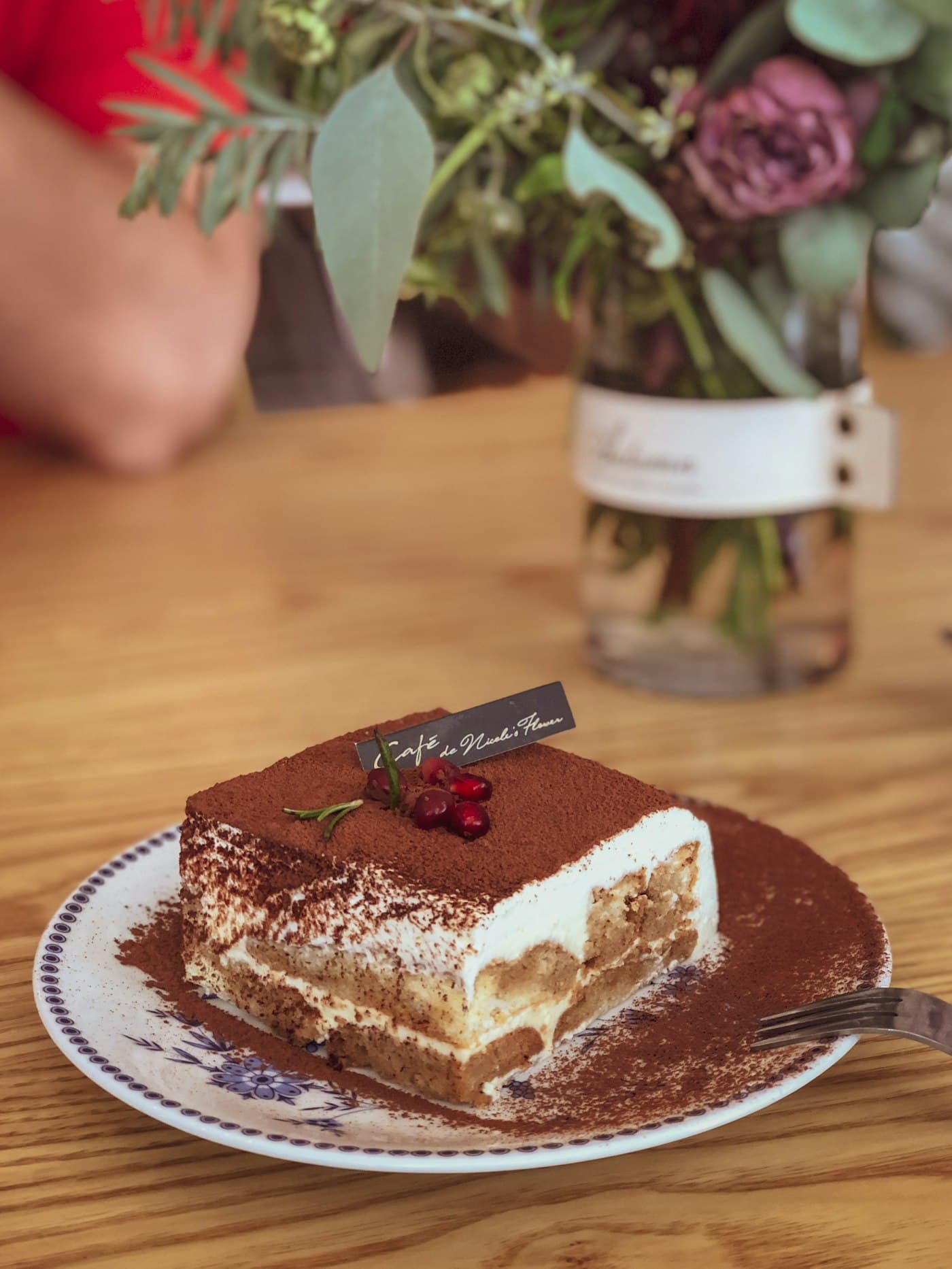 A slice of tiramisu dusted with cocoa on a plate on a walnut table
