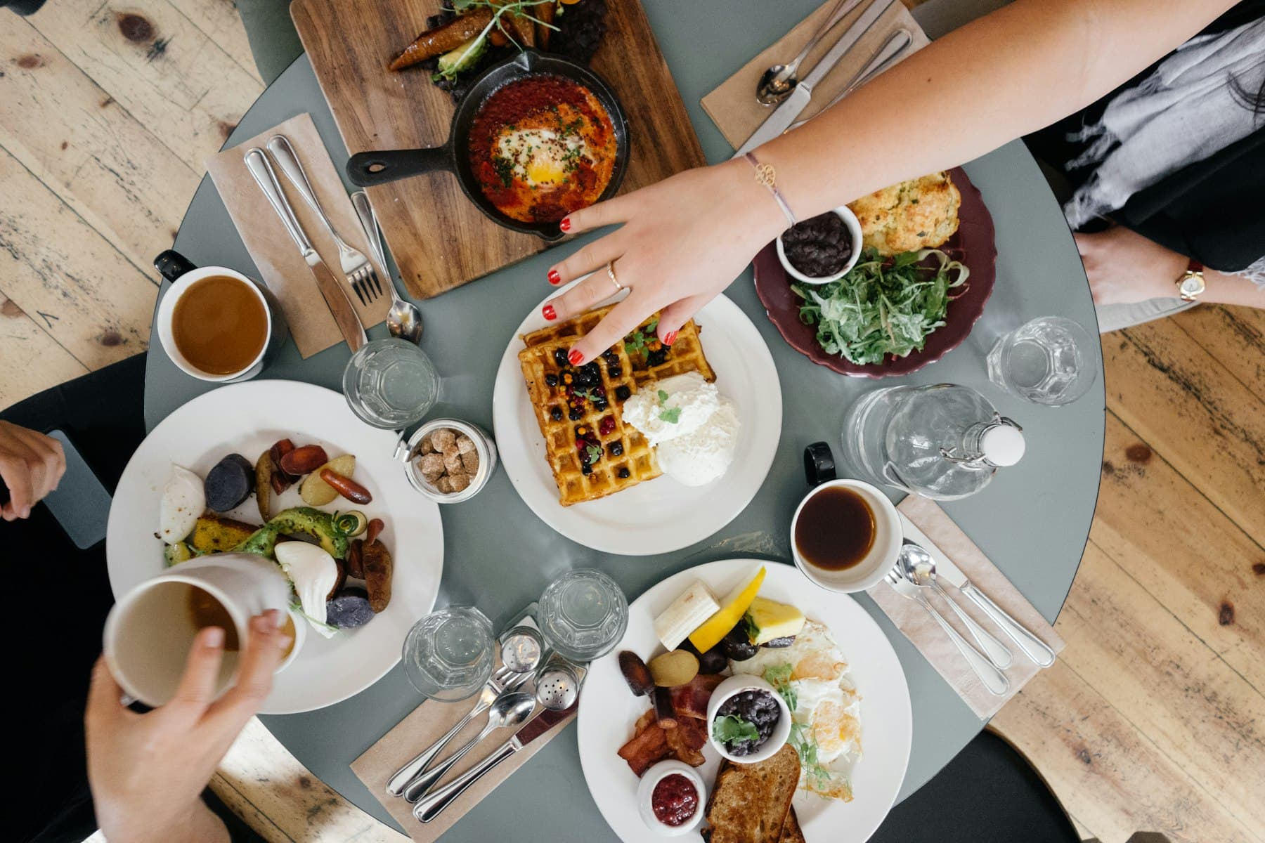 A shared brunch table seen from above with coffee, waffles and fruit
