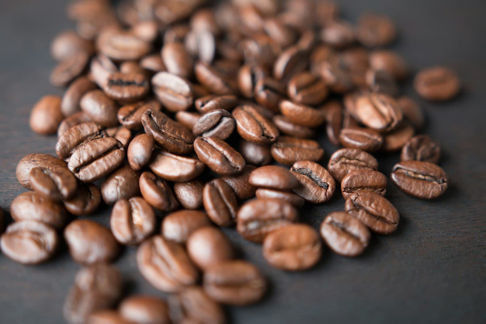 Roasted coffee beans scattered across a dark surface