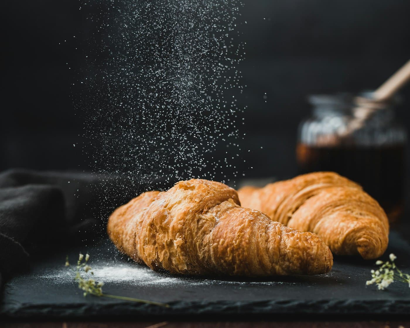 A croissant dusted with icing sugar, lit from the side