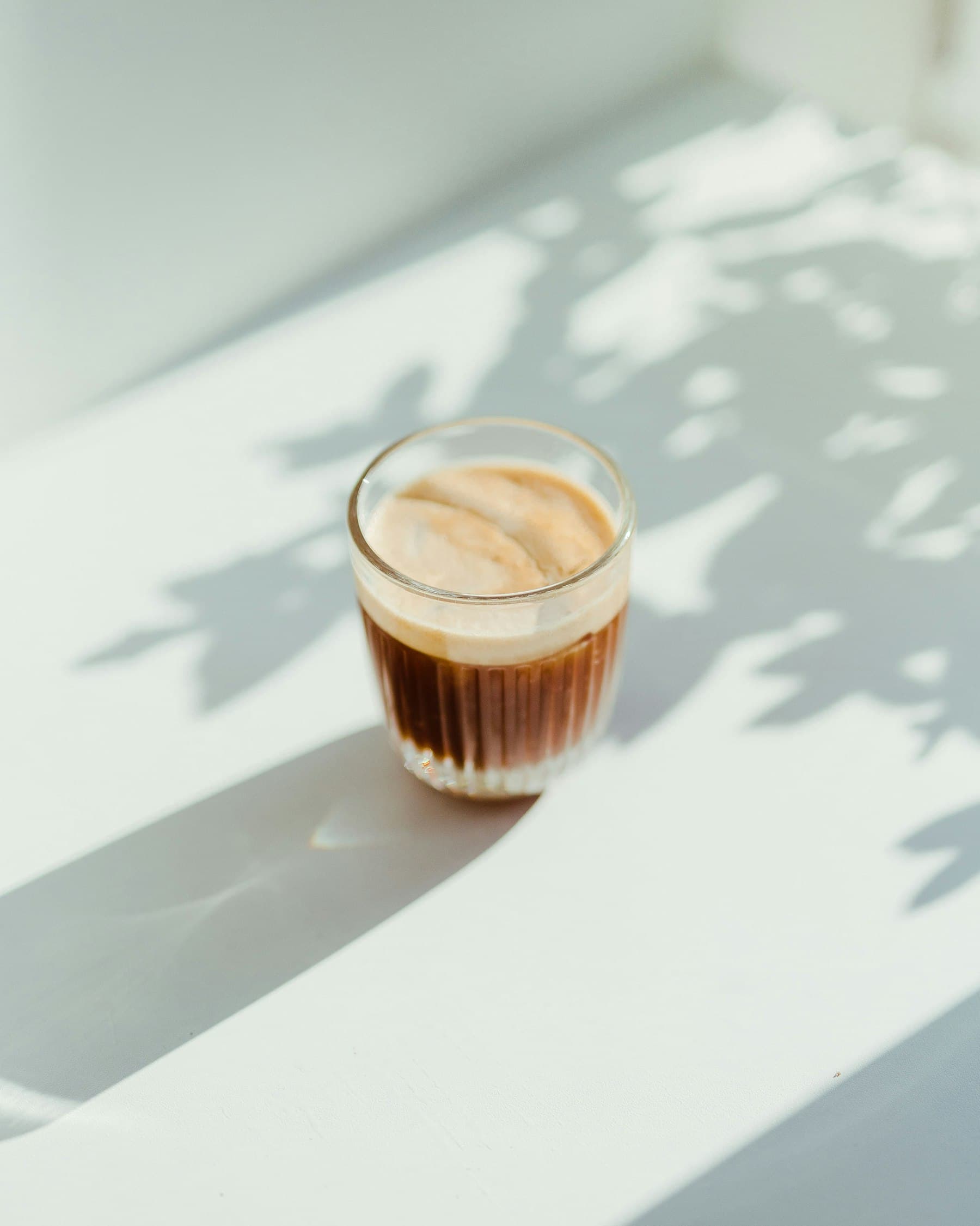 An espresso glass in low morning light with leaf shadows