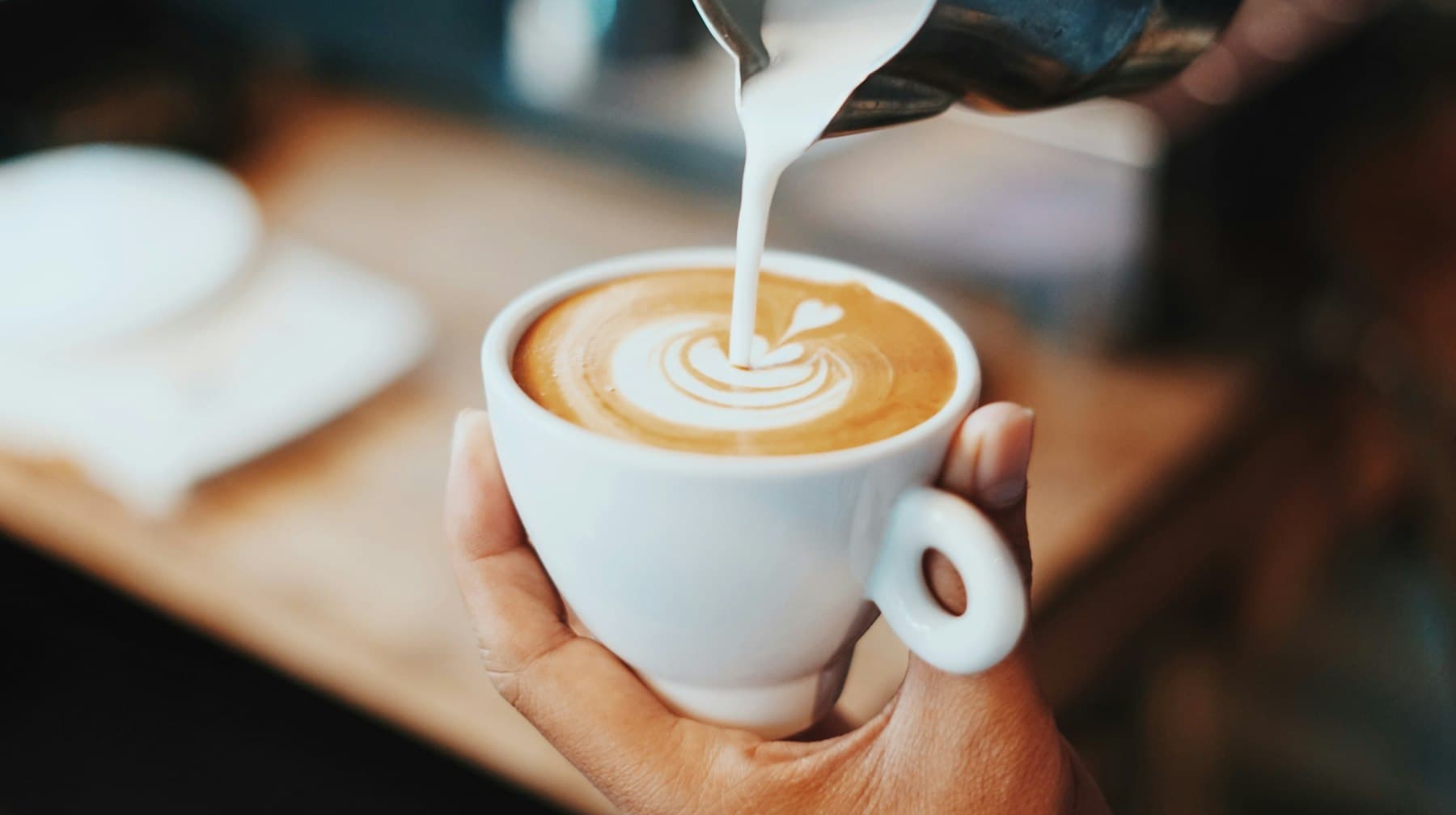 Steamed milk poured into a Spanish latte, forming latte art in a white cup